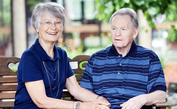 Husband and wife sitting together on a bench outdoors at Traditions at Bridgepointe Gardens in Jeffersonville, Indiana.